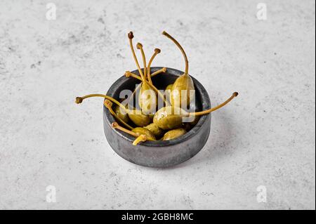 Capperi marinati in ciotola su fondo testurizzato chiaro. Primo piano. Spazio libero per il testo Foto Stock