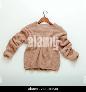 Pullover beige lavorato a maglia su appendiabiti. Il pullover in cashmere vola piatto su sfondo bianco. Caldo ed elegante abito invernale marrone caldo pullover lavorato a maglia Foto Stock