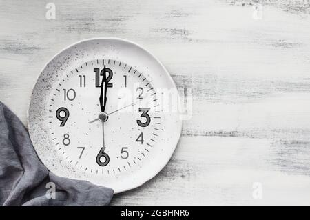 Posa piatta di un orologio a piatto bianco con tovagliolo su un tavolo rustico in legno con spazio copia per il concetto di digiuno intermittente. Foto Stock