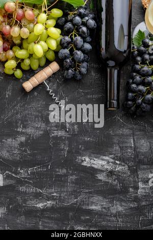 Bottiglia di vino e cavatappi di tipo diverso su fondo nero. Composizione minimalistica di vino rosso a moody scuro su tavola di pietra. Telaio piatto Foto Stock