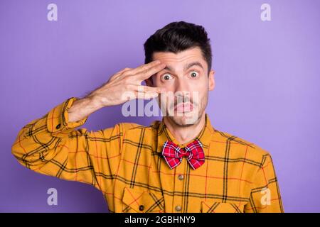 Foto di giovane uomo eccitato childish stolante grimacing dita vicino occhio isolato su sfondo di colore viola Foto Stock