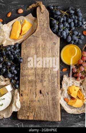 Tagliere in legno vintage vuoto al centro del telaio fatto di uva da miele formaggio snack altri ingredienti gastronomia spuntini. Simulazione dello spazio di copia o. Foto Stock