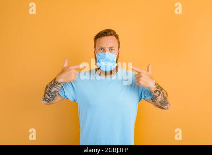 L'uomo arrabbiato con barba e tatuaggi vuole rimuovere la maschera per covid-19 Foto Stock