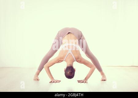 Ritratto di splendida sportiva attiva giovane donna a praticare yoga in studio. Bella ragazza pratica Dandayamana Bibhaktapada Paschimotthanasana Foto Stock