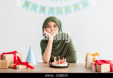 Unappy ragazza teen indiana in hijab avendo festa di compleanno opaca, festeggiando da sola la vacanza durante il blocco covid, indoor Foto Stock