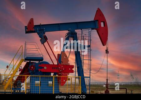 Un carro di perforazione petrolifero pompa olio sullo sfondo di un tramonto rosso e di un bel cielo. Foto Stock