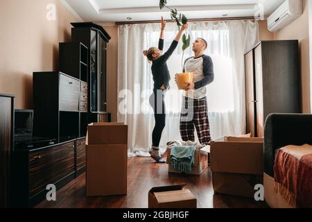 Giorno in movimento, passa a Nuova casa. Giovane coppia felice, famiglia newlyweds che si diverte in camera con piante di casa e scatole di cartone preparati per muoversi in o. Foto Stock