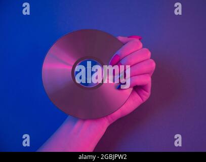 Compact disc in luce al neon viola e mano femminile con manicure retrovonda. Foto Stock