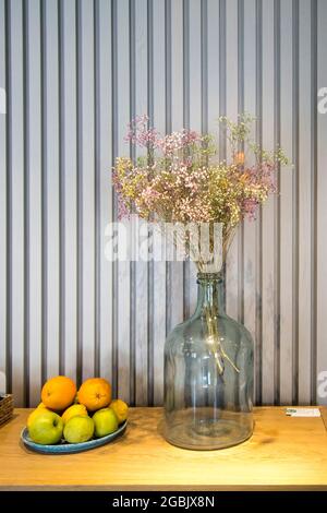 Un bouquet di gypsophila essiccata dipinta multicolore in una grande  bottiglia di vetro invece di un vaso come decorazione da tavolo. Ciotola  con arance e limoni Foto stock - Alamy