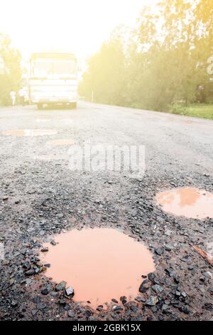 Una strada di ghiaia bagnata e accidentata dopo la pioggia. Una strada in ghiaia è piena di buche. Una strada di campagna nel sud della Cambogia. Mettere a fuoco il pootolo in primo piano. Foto Stock