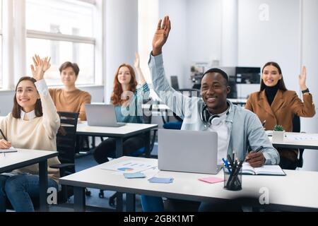 Ritratto di diversi studenti che alzano le mani in classe moderna Foto Stock