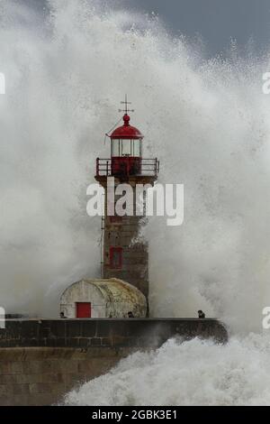 Porto, Portogallo - 7 febbraio 2016: Grandi onde oceaniche contro il vecchio faro e molo in un pomeriggio tempestoso vedere le persone in fuga. Foto Stock