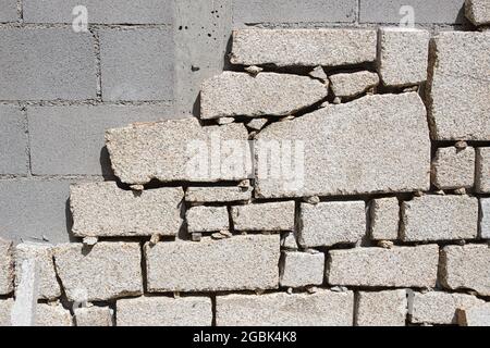 Particolare della parete del blocco di Cinder essendo rivestita con lastre di granito in cantiere esterno. Decorazione della parete Foto Stock