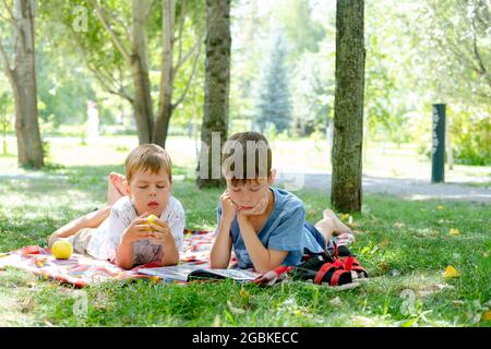 Due ragazzi si stendono su una coperta in un parco verde. I bambini leggono un libro sdraiato a terra, nel parco. Bambini in un pic-nic in estate, la lettura di libri. S Foto Stock