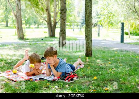 Due ragazzi si stendono su una coperta in un parco verde. I bambini leggono un libro sdraiato a terra, nel parco. Bambini in un pic-nic in estate, la lettura di libri. S Foto Stock