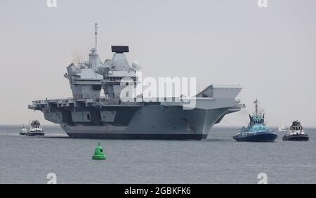 I Tugs guidano la portaerei della Royal Navy HMS PRINCE OF WALES verso la base navale Foto Stock