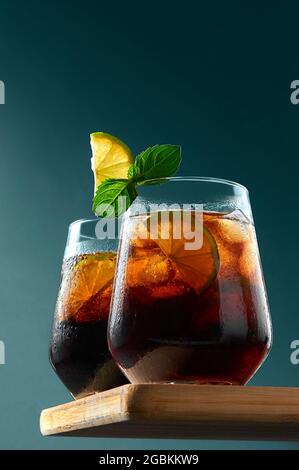 Cuba Libre o Long Island cocktail con rum, cola e lime in bicchieri su tavola di legno su sfondo blu scuro. Rinfrescante bevanda estiva. Foto Stock