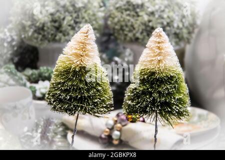 Esposizione da tavolo da sogno di due alberi di bottlebrush con porta perle su tovagliolo e verde di Natale sfocato sullo sfondo. Foto Stock