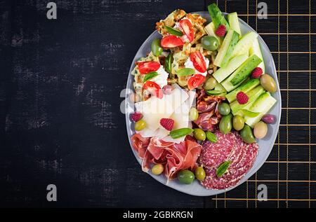 Lavagna di salumi. Piatto: parmigiano con prosciutto, salame, cetrioli e olive. Assortimento di gustosi antipasti o antipasti. Vista dall'alto, spazio di copia, Foto Stock