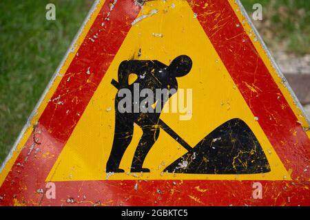 Vecchio segno giallo del triangolo stradale graffiato sui lavori di costruzione Foto Stock