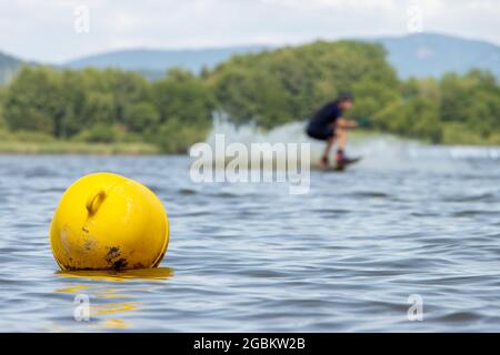 Una boa gialla galleggia su una superficie d'acqua in un lago con un surfista sullo sfondo. Foto Stock