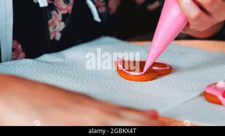 Processo di decorazione di biscotti a forma di cuore con glassa di zucchero rosa. Cibo di vacanza fare. Foto Stock