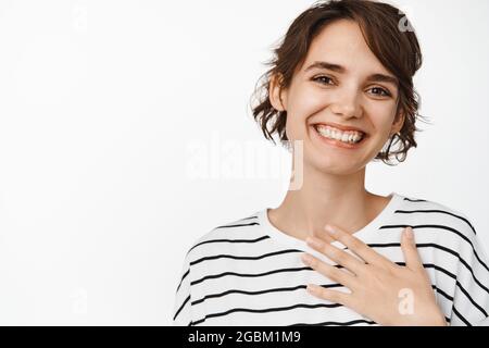 Grazie. Felice sorridente ragazza tenere la mano sul cuore, guardando lusingato, essendo grato e soddisfatto, in piedi su sfondo bianco Foto Stock