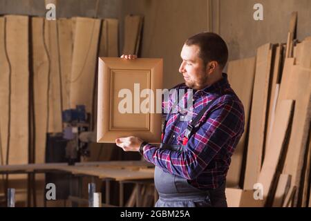 il falegname nei vestiti di lavoro guarda un proprio prodotto Foto Stock