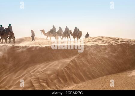 Vista dei turisti che cavalcano i cammelli nel deserto del Sahara durante i forti venti Foto Stock