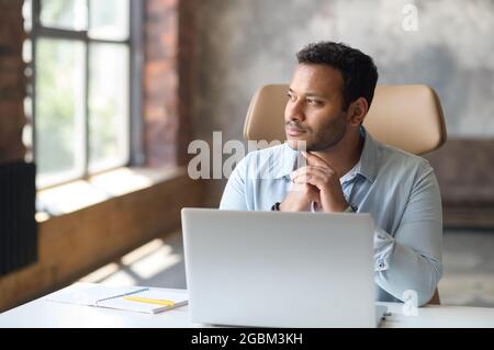 Serio concentrato intelligente professionista indiano utilizzando il computer portatile per la ricerca, cercando perso nella ricerca di idee per l'avvio, un lavoro premuroso millennial in remoto a casa Foto Stock