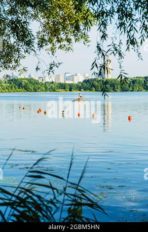 Stand up paddle boarding. Gruppo di persone che navigano a bordo di pagaia vicino alle boe arancioni sul lago, fiume, vicino alla città. Concetto di vacanza estiva Foto Stock