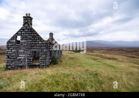 Il guscio rovinato di un piccolo cottage si erge da solo nel vasto paesaggio di torbiere di Rannoch Moor nelle Highlands della Scozia. Foto Stock