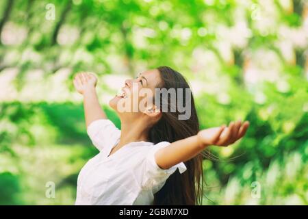 Donna felice respirare aria fresca pulita all'aperto foresta naturale per la stagione primaverile allergie polline. Ragazza asiatica spensierata con braccia distese in libertà Foto Stock