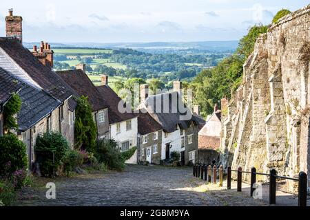 I cottage tradizionali fiancheggiano la pittoresca strada acciottolata di Gold Hill sopra il Blackmore vale a Shaftedbury, Dorset. Foto Stock