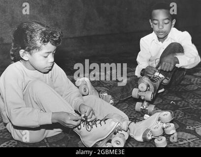 Luling Texas USA, circa 1985: Black boy and girl stringono scarpe da pattinaggio a rotelle sulla pista di pattinaggio interna. ©Bob Daemmrich Foto Stock