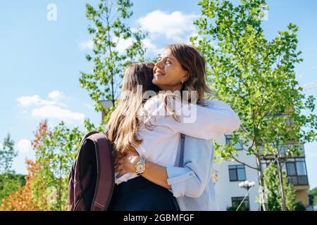 Ragazza pupilla con zaino e uniforme che abbraccia la madre prima di andare a scuola. Foto Stock