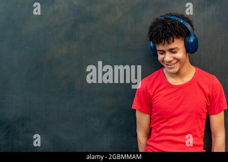 Afro latino maschio adolescente ascolto di musica contro un muro Foto Stock