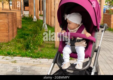 la bambina si siede in un passeggino e vuole andare da sola Foto Stock