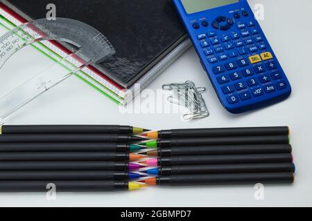 gruppo di strumenti scolastici con notebook, pennarelli, penne, clip, calcolatrice e regole pronte per il ritorno a scuola su sfondo bianco Foto Stock