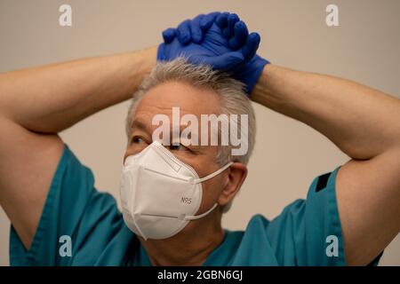 Medico che riposa le mani sopra la testa mostrando l'espressione stanca Foto Stock