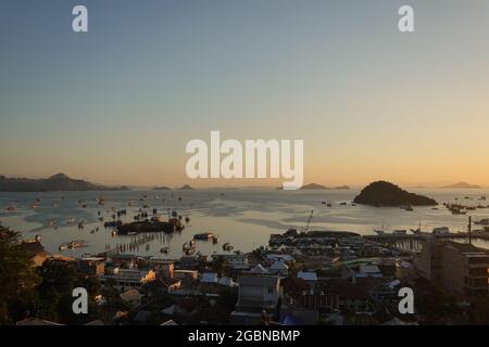 Tramonto sulla città e il porto di Labuan Bajo, con molte navi da crociera tradizionali Phinisi ancorate come la città è il punto di ingresso al Komodo nazionale Foto Stock