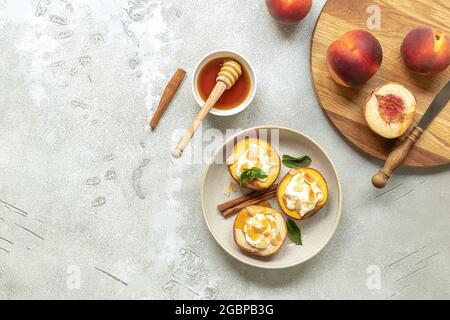 Pesche mature al forno con cannella, petali di mandorle, formaggio cremoso e miele su un fondo di cemento chiaro. Foto Stock