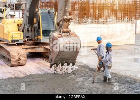 Operaio di costruzioni con macchina pesante dell'escavatore per la colata del calcestruzzo durante i pavimenti commerciali di calcestruzzo dell'edificio in cantiere Foto Stock