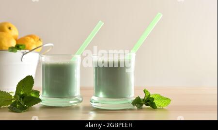 Due bicchieri con latte alla menta su tavolo di legno con secchio con limoni e fondo isolato. Vista frontale. Foto Stock