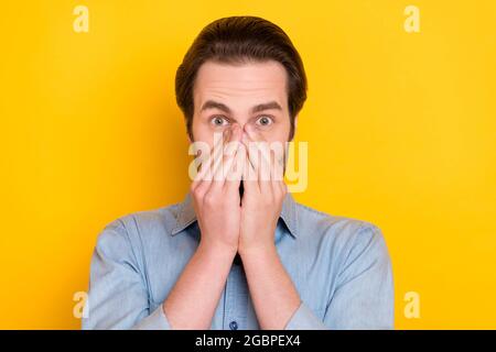 Ritratto fotografico di un ragazzo stupito coperto faccia con le mani che indossano una camicia jeans isolato su uno sfondo di colore giallo brillante Foto Stock