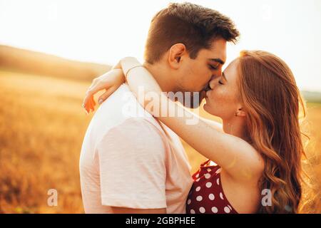 Primo piano foto di una donna zenzero con freccelle che baciano il suo amante in un campo soleggiato di grano che abbraccia Foto Stock