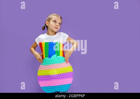 Sorprendo il bambino che tiene enorme mela anti bolla di stress. Abilità motorie. Pop it divertente. Bambino che tiene colore popit fidget Foto Stock