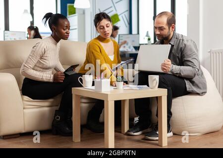 Team di colleghi creativi e amichevoli che discutono del progetto aziendale utilizzando notebook e tablet sul posto di lavoro. Gruppo di collaboratori multirazziali che lavorano insieme condividendo idee di marketing durante la riunione d'ufficio Foto Stock