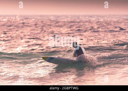 Un membro del Newquay Surf Lifesaving Club che cavalca una tavola di salvataggio Vanquish durante una sessione di allenamento al Fistral di Newquay in Cornovaglia. Foto Stock