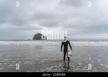 Un solista maschile in una tuta bagnata si dirige verso il surf per catturare un'onda a Trebarwith Strand nel Nord Cornovaglia. Foto Stock